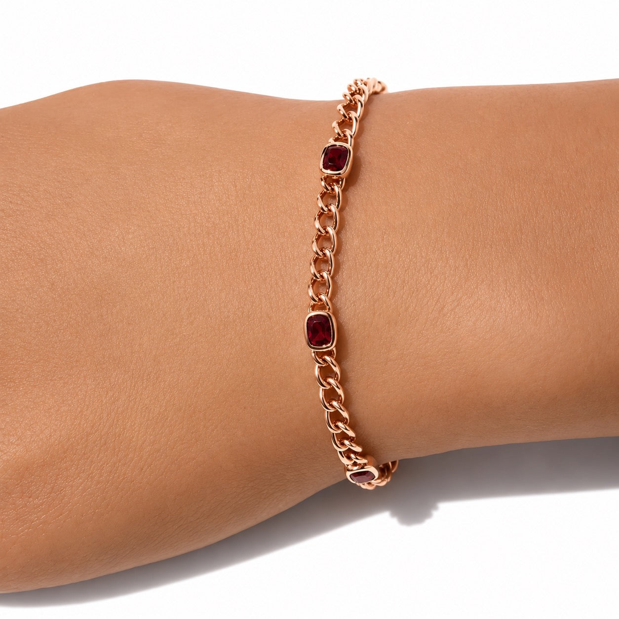 A rose gold chain bracelet featuring cushion-cut rubies set in bezels, shown on a wrist.