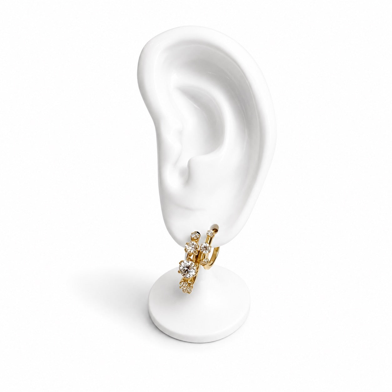 A gold huggie hoop earring with white diamonds, displayed on a white ear-shaped stand against a white background.