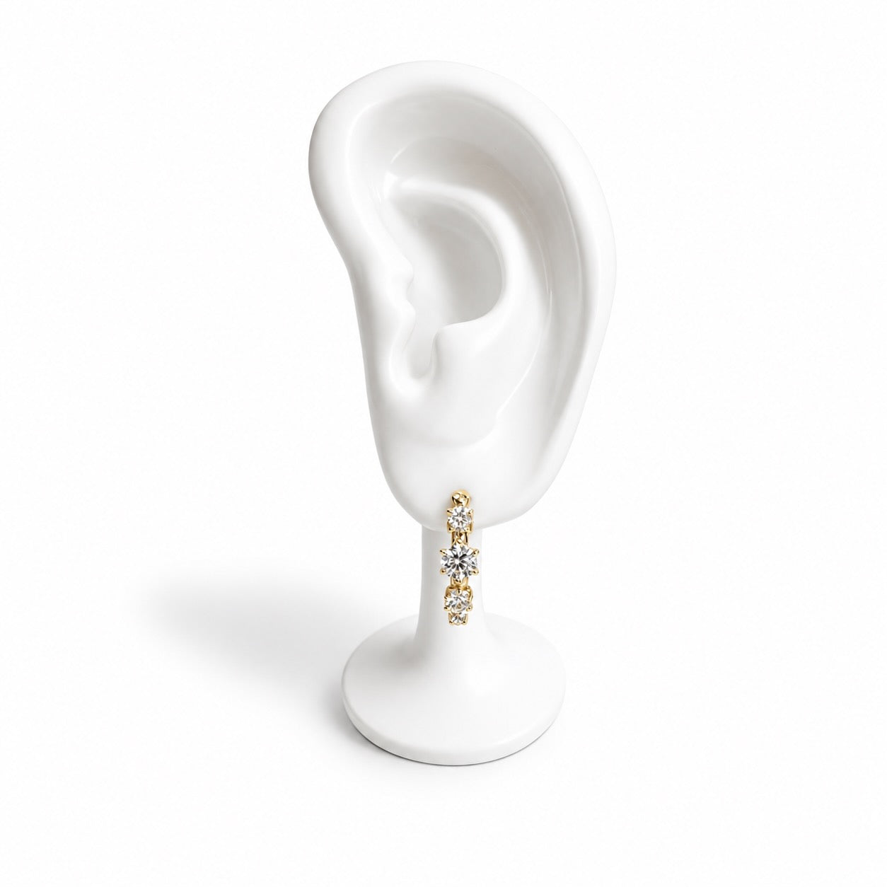 A gold and diamond hoop earring displayed on a white ceramic ear-shaped stand against a white background.